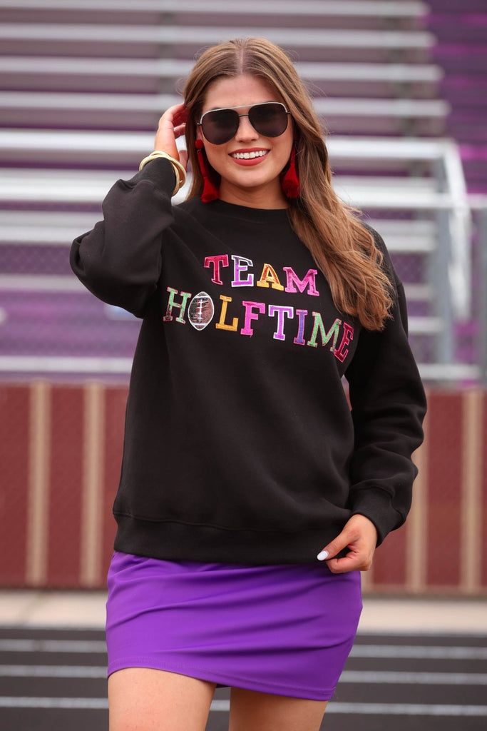 black long sleeve sweatshirt made from a midweight, soft material fabric with a crew neckline, straight hemline, and multicolored letter patches spelling out TEAM HALFTIME&nbsp;on the front