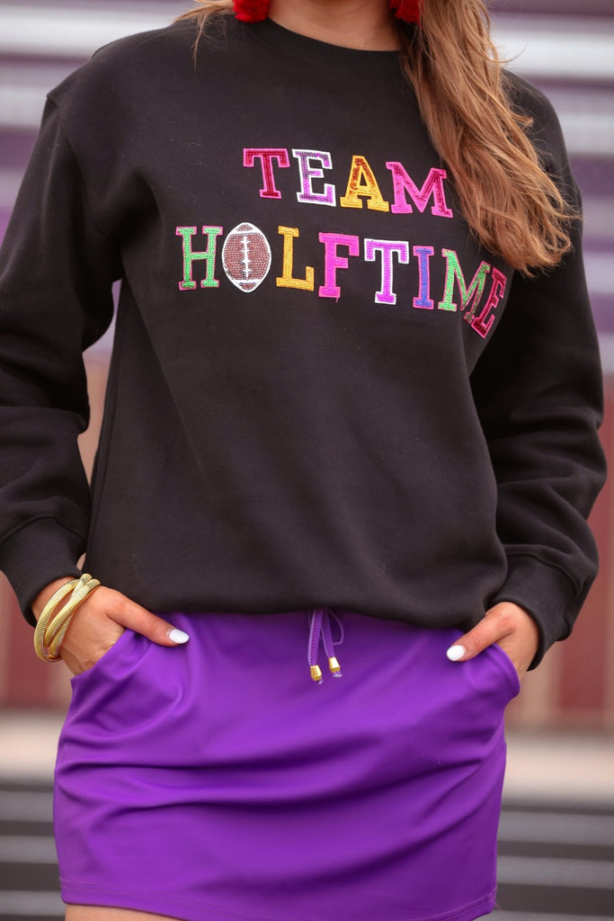 black long sleeve sweatshirt made from a midweight, soft material fabric with a crew neckline, straight hemline, and multicolored letter patches spelling out TEAM HALFTIME&nbsp;on the front