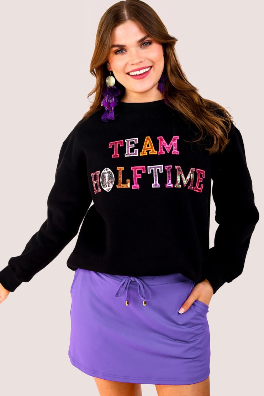 black long-sleeve sweatshirt made from soft mid-weight fabric with a crew neckline, straight hem, and bold multicolored varsity-style chenille patches that spell out 'TEAM HALFTIME' across the front chest