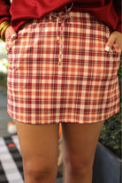 mid-rise relaxed fit everyday skort made of lightweight material with built-in cream shorts, drawstring tie with gold bead accents, an elastic band on the back, and side pockets, designed on a burgundy, ivory, and orange plaid pattern
