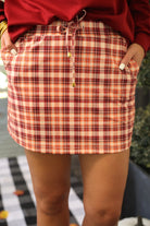 mid-rise relaxed fit everyday skort made of lightweight material with built-in cream shorts, drawstring tie with gold bead accents, an elastic band on the back, and side pockets, designed on a burgundy, ivory, and orange plaid pattern