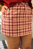 mid-rise relaxed fit everyday skort made of lightweight material with built-in cream shorts, drawstring tie with gold bead accents, an elastic band on the back, and side pockets, designed on a burgundy, ivory, and orange plaid pattern