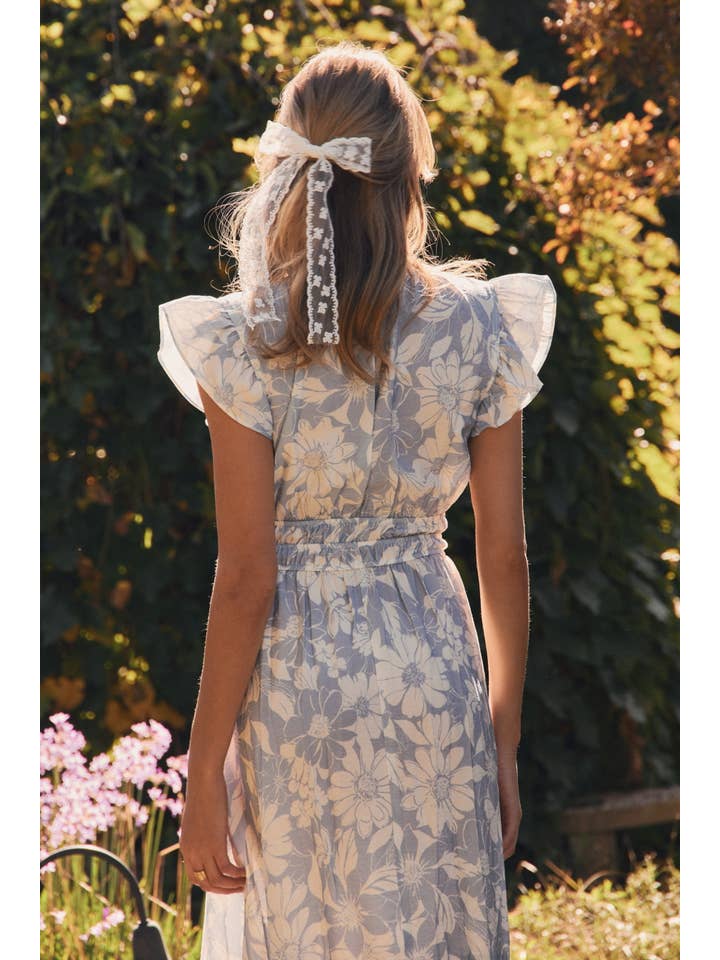 Woman in a floral dress standing outdoors with greenery and flowers in the background
