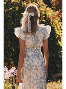 Woman in a floral dress standing outdoors with greenery and flowers in the background