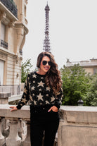 a black long-sleeve crewneck sweater with a festive star motif, shimmering tinsel woven throughout, and ribbed trim at the neckline, cuffs, and hemline