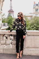 a black long-sleeve crewneck sweater with a festive star motif, shimmering tinsel woven throughout, and ribbed trim at the neckline, cuffs, and hemline
