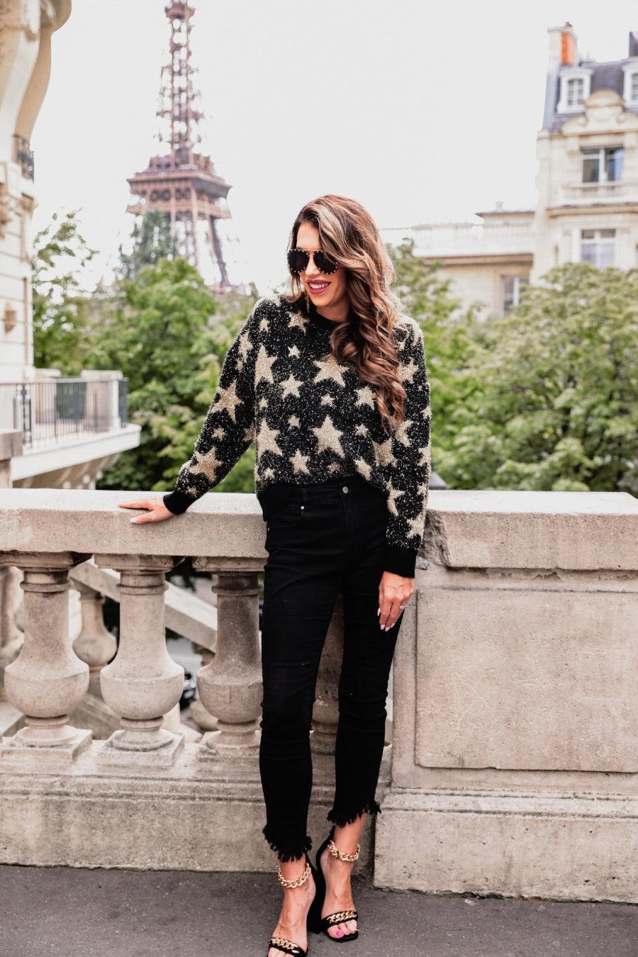 a black long-sleeve crewneck sweater with a festive star motif, shimmering tinsel woven throughout, and ribbed trim at the neckline, cuffs, and hemline