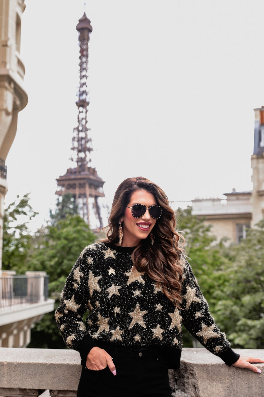 a black long-sleeve crewneck sweater with a festive star motif, shimmering tinsel woven throughout, and ribbed trim at the neckline, cuffs, and hemline