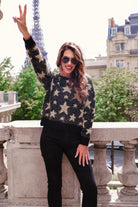 a black long-sleeve crewneck sweater with a festive star motif, shimmering tinsel woven throughout, and ribbed trim at the neckline, cuffs, and hemline