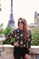 a black long-sleeve crewneck sweater with a festive star motif, shimmering tinsel woven throughout, and ribbed trim at the neckline, cuffs, and hemline