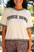 a boxy fit crew neck tee with a leopard 'TOUCH DOWN' fabric patch, embroidered outline, contrast neckline and sleeve trim, short sleeves, and soft stretch fabric on a cream base