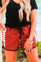 mid-rise relaxed fit activewear shorts with side pockets and a tie waist drawstring with gold bead accent, designed with a football-lace inspired pattern print fabric down each leg, brown base, and black trim