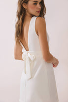 a white sleeveless mini dress with a deep V-neckline, wide waistband, dramatic low back, and self-tie bow detail