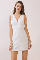 a white sleeveless mini dress with a deep V-neckline, wide waistband, dramatic low back, and self-tie bow detail