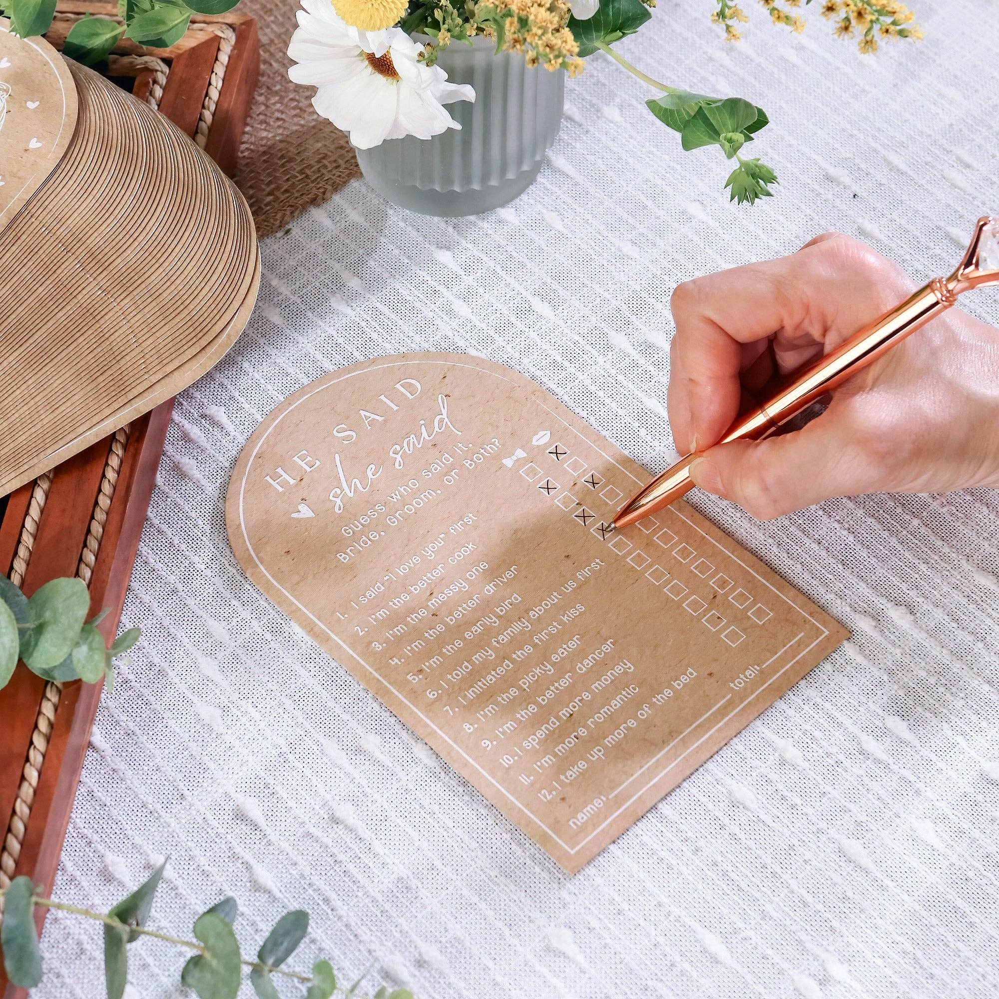 Hand writing on a personalized card with a rose gold pen, surrounded by decorative elements.