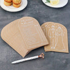 Two wedding-themed cards on a dark surface with a pen and plates of muffins and lemon slices in the background.