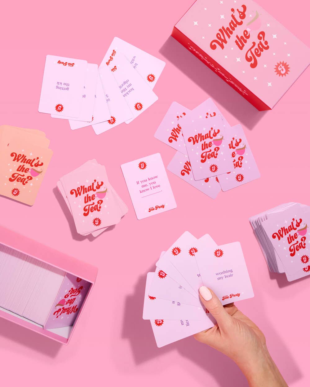 Card game 'What's the Tea?' with cards and packaging on a pink background