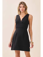 a black sleeveless mini dress with a deep V-neckline, wide waistband, dramatic low back, and self-tie bow detail