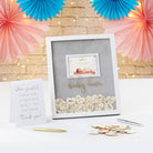 Decorative baby shower frame with heart-shaped confetti and a card on a table with festive decorations.