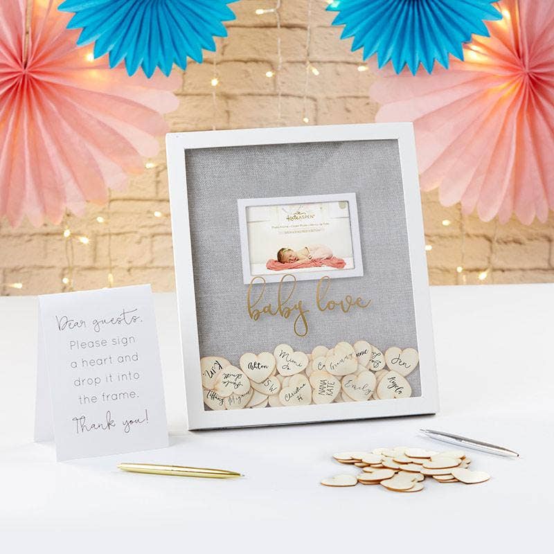 Decorative baby shower frame with heart-shaped confetti and a card on a table with festive decorations.