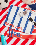 a soft lightweight square polyester bandana with a red, white, and blue flag-inspired print, stars, strips, Team USA lettering, and versatile styling options