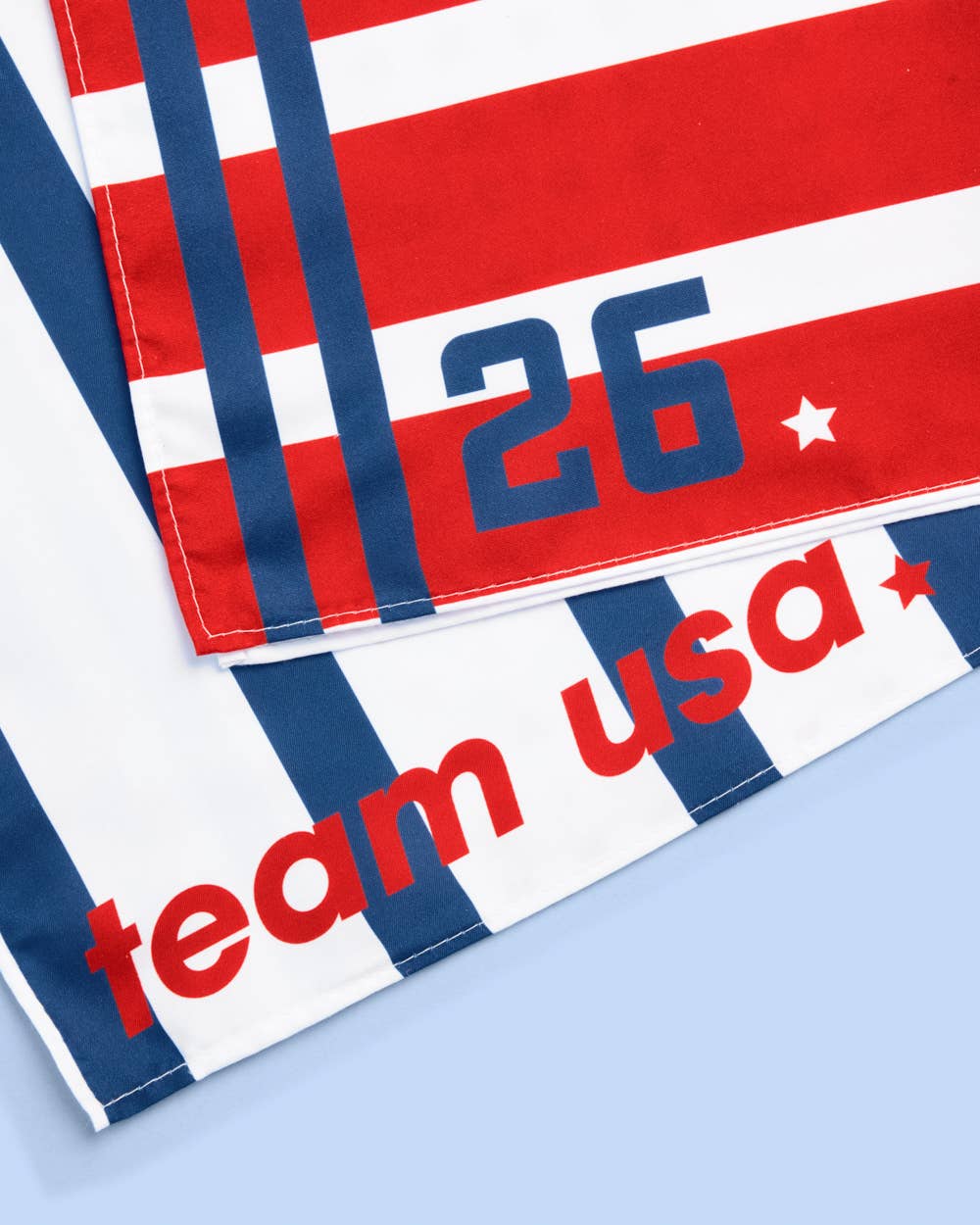 a soft lightweight square polyester bandana with a red, white, and blue flag-inspired print, stars, strips, Team USA lettering, and versatile styling options