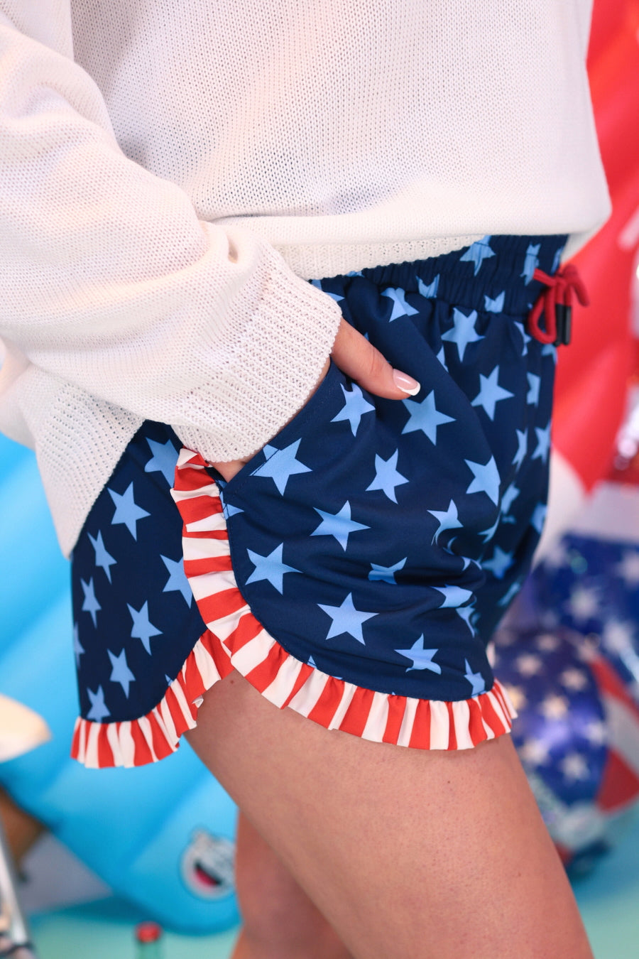 mid-rise relaxed fit activewear shorts with side pockets and a red tie waist drawstring finished with black aglets, designed on a two-tone blue star pattern print and red-and-white ruffle trim