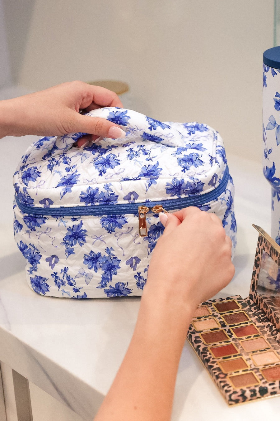 a structured bag with a spacious interior, a secure double zip around closure, a top handle, and gold accents on a quilted body in blue blossom (white/blue)