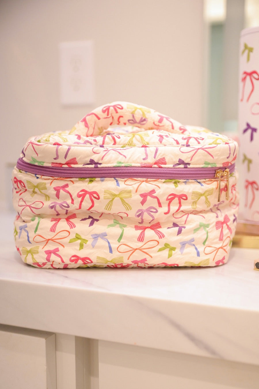 a structured bag with a spacious interior, a secure double zip around closure, a top handle, and gold accents on a quilted body in daylight bow (multi)