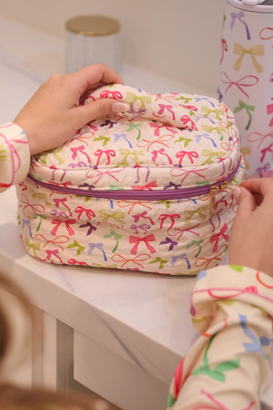 a structured bag with a spacious interior, a secure double zip around closure, a top handle, and gold accents on a quilted body in daylight bow (multi)