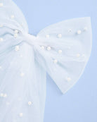 Large white bow with pearl-like embellishments on a light blue background