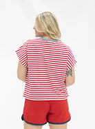 a high-stretch oversized short-sleeve stripe top with a crew neckline, a horizontal stripe pattern (red and white), bold denim 1776 patch detail, tiny star accents, a relaxed easy drape, and unlined