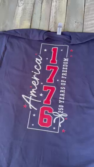 a soft navy unisex Gildan t-shirt with a crew neckline, short sleeves, a front America 250 chest graphic, a bold 1776 America back design, a 250 Years of Freedom detail, and an easy year-round fit