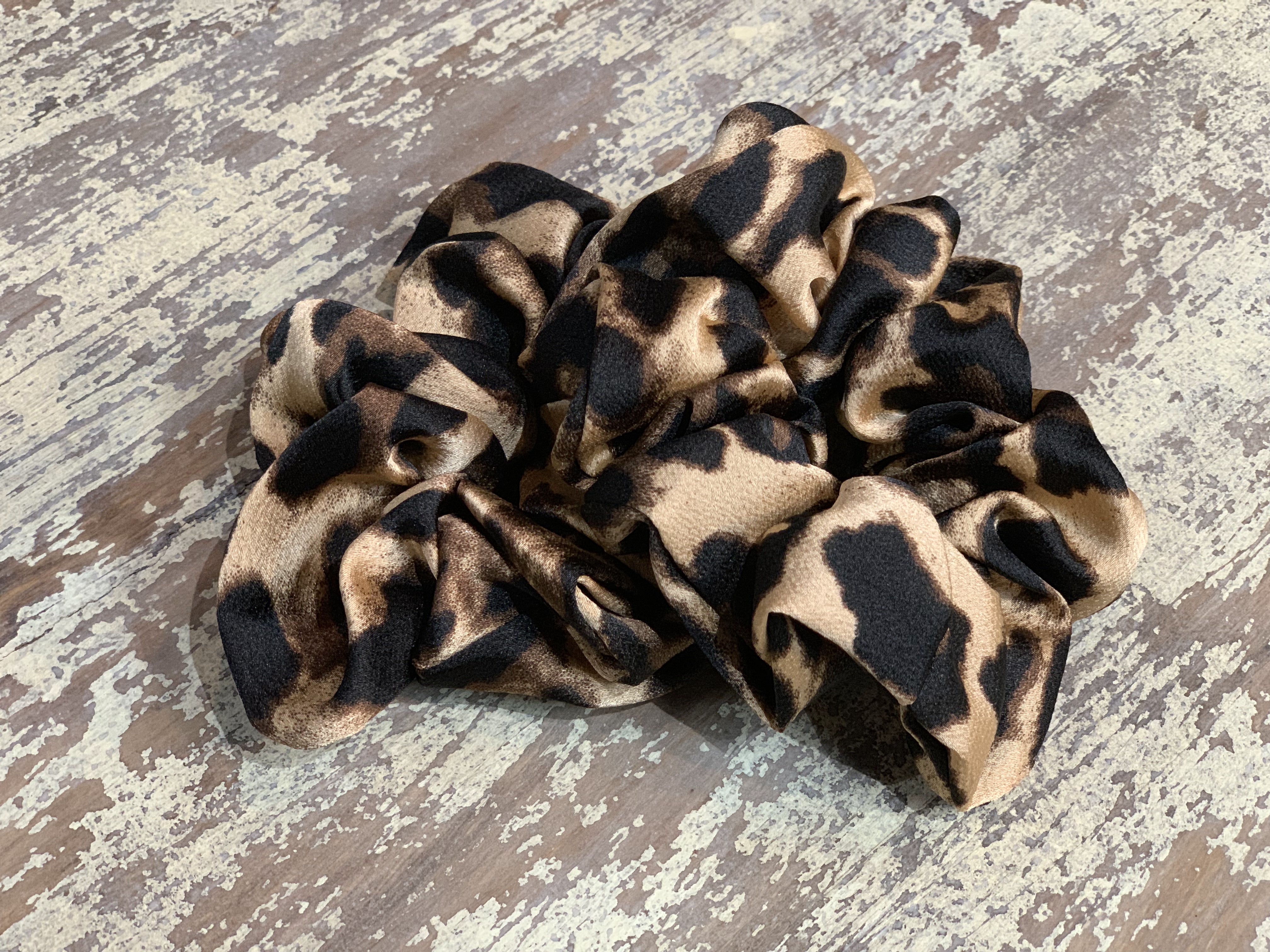 an oversized satin-look leopard scrunchie with glossy animal print fabric, plush gathered construction, lightweight feel, and gentle hair-friendly hold in leopard beige