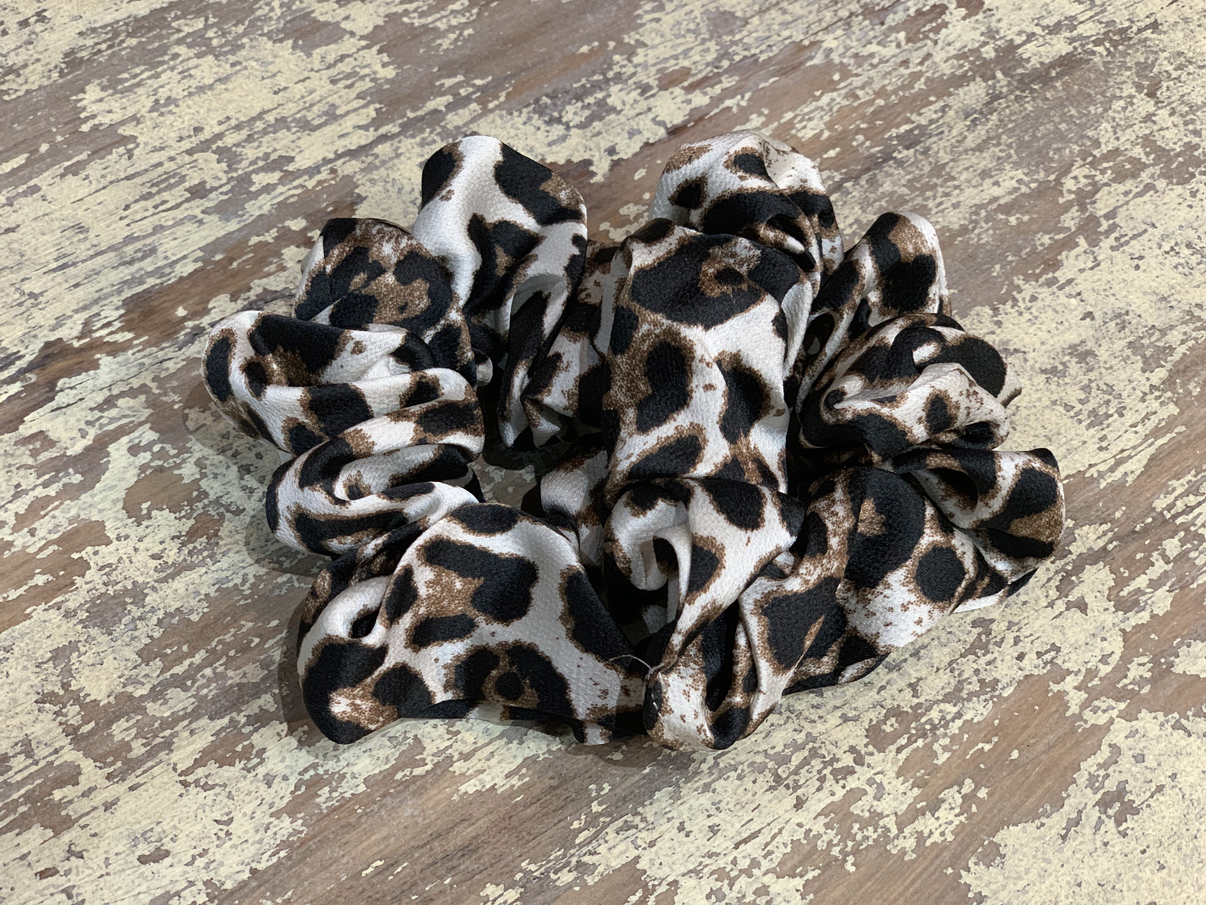 an oversized satin-look leopard scrunchie with glossy animal print fabric, plush gathered construction, lightweight feel, and gentle hair-friendly hold in leopard white