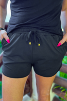 mid-rise relaxed fit activewear shorts with side pockets and a tie waist drawstring with gold bead accents, designed on a solid black print fabric and black trim