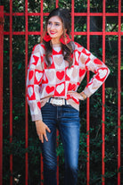 a long-sleeve crew neckline sweater with a relaxed drop-shoulder silhouette and ribbed hemline, neckline, and cuffs, plus a contrasting color block heart pattern in ivory, red, and taupe