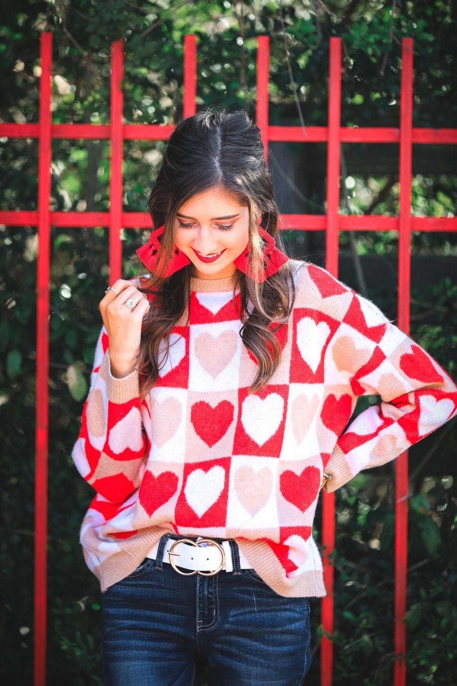 a long-sleeve crew neckline sweater with a relaxed drop-shoulder silhouette and ribbed hemline, neckline, and cuffs, plus a contrasting color block heart pattern in ivory, red, and taupe