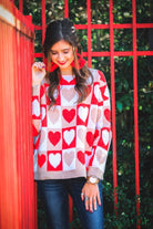 a long-sleeve crew neckline sweater with a relaxed drop-shoulder silhouette and ribbed hemline, neckline, and cuffs, plus a contrasting color block heart pattern in ivory, red, and taupe