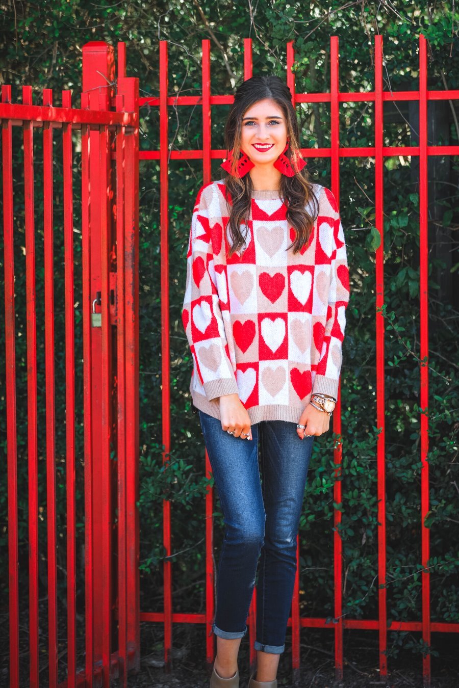 a long-sleeve crew neckline sweater with a relaxed drop-shoulder silhouette and ribbed hemline, neckline, and cuffs, plus a contrasting color block heart pattern in ivory, red, and taupe
