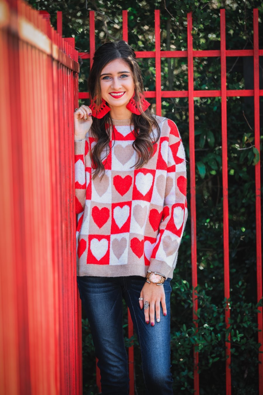 a long-sleeve crew neckline sweater with a relaxed drop-shoulder silhouette and ribbed hemline, neckline, and cuffs, plus a contrasting color block heart pattern in ivory, red, and taupe