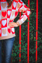 a long-sleeve crew neckline sweater with a relaxed drop-shoulder silhouette and ribbed hemline, neckline, and cuffs, plus a contrasting color block heart pattern in ivory, red, and taupe