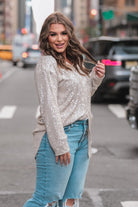 a loose long-sleeve top made of lightweight material covered in shimmering sequins with a collared neckline, fitted button closure cuffs, an accent chest pocket, and a relaxed button-up silhouette that falls into a round high-low hemline in champagne