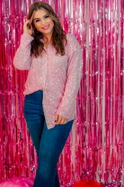 a loose long-sleeve top made of lightweight material covered in shimmering sequins with a collared neckline, fitted button closure cuffs, an accent chest pocket, and a relaxed button-up silhouette that falls into a round high-low hemline in pink