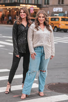 a loose long-sleeve top made of lightweight material covered in shimmering sequins with a collared neckline, fitted button closure cuffs, an accent chest pocket, and a relaxed button-up silhouette that falls into a round high-low hemline in black and champagne 