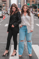 a loose long-sleeve top made of lightweight material covered in shimmering sequins with a collared neckline, fitted button closure cuffs, an accent chest pocket, and a relaxed button-up silhouette that falls into a round high-low hemline in black and champagne