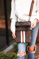 spacious crossbody bag in a black and brown leopard print made of neoprene with an adjustable strap (tonal brown), two front pockets (one zipper, one open), and racing stripes (brown and white) on a black and brown leopard print pattern