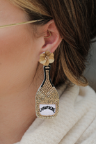 a gold flower stud with black, gold, and white beads in the shape of a champagne bottle