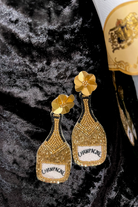 a gold flower stud with black, gold, and white beads in the shape of a champagne bottle