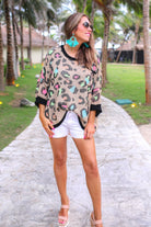 three quarter cuffed sleeve sweater made from unlined loose knit material with a rounded neckline, a chest pocket, and an oversized fit on a multicolor leopard pattern (blue, green, pink, and orange), a black accent color (chest pocket trim, cuffs, and hem), and a brown base